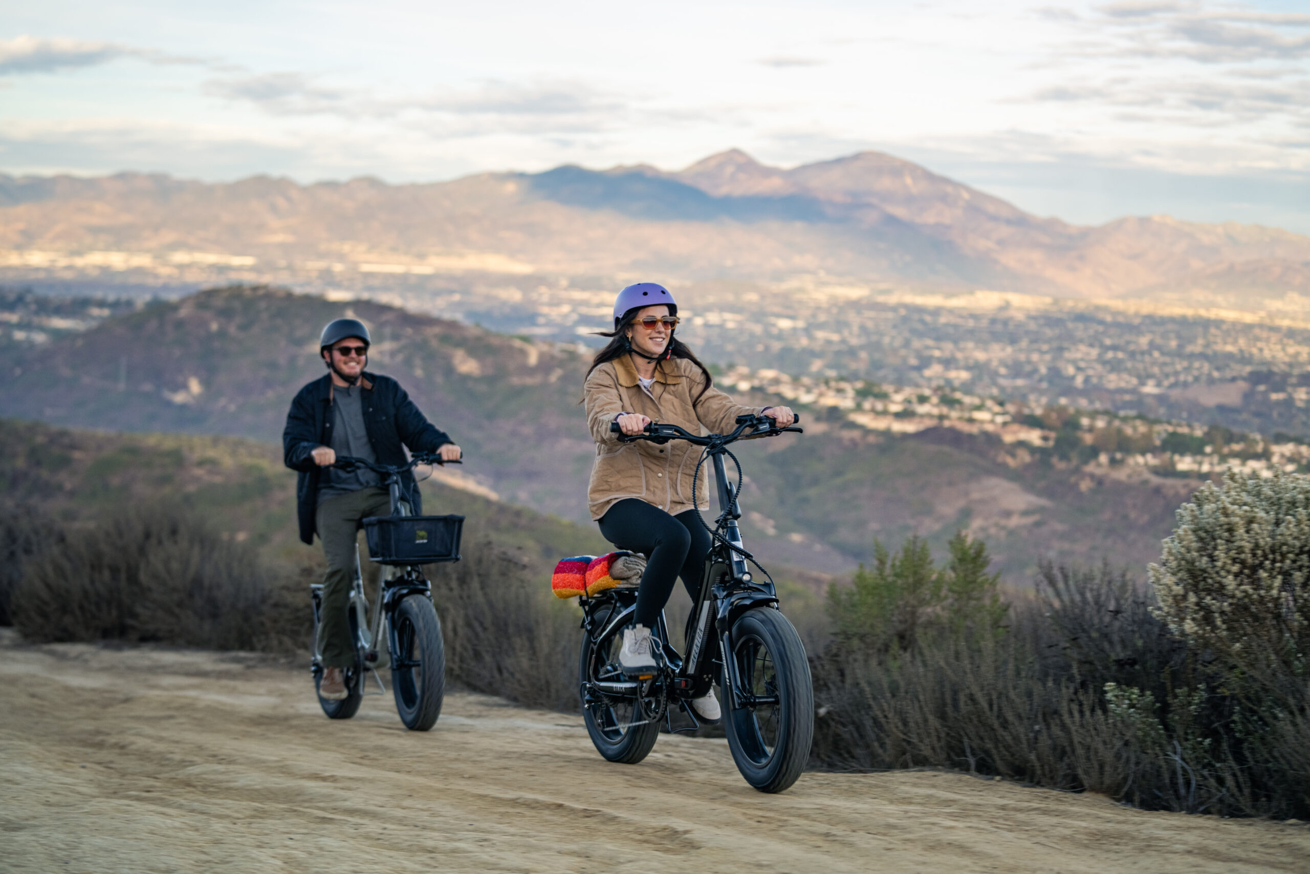 a man and woman riding e-bikes on a dirt road