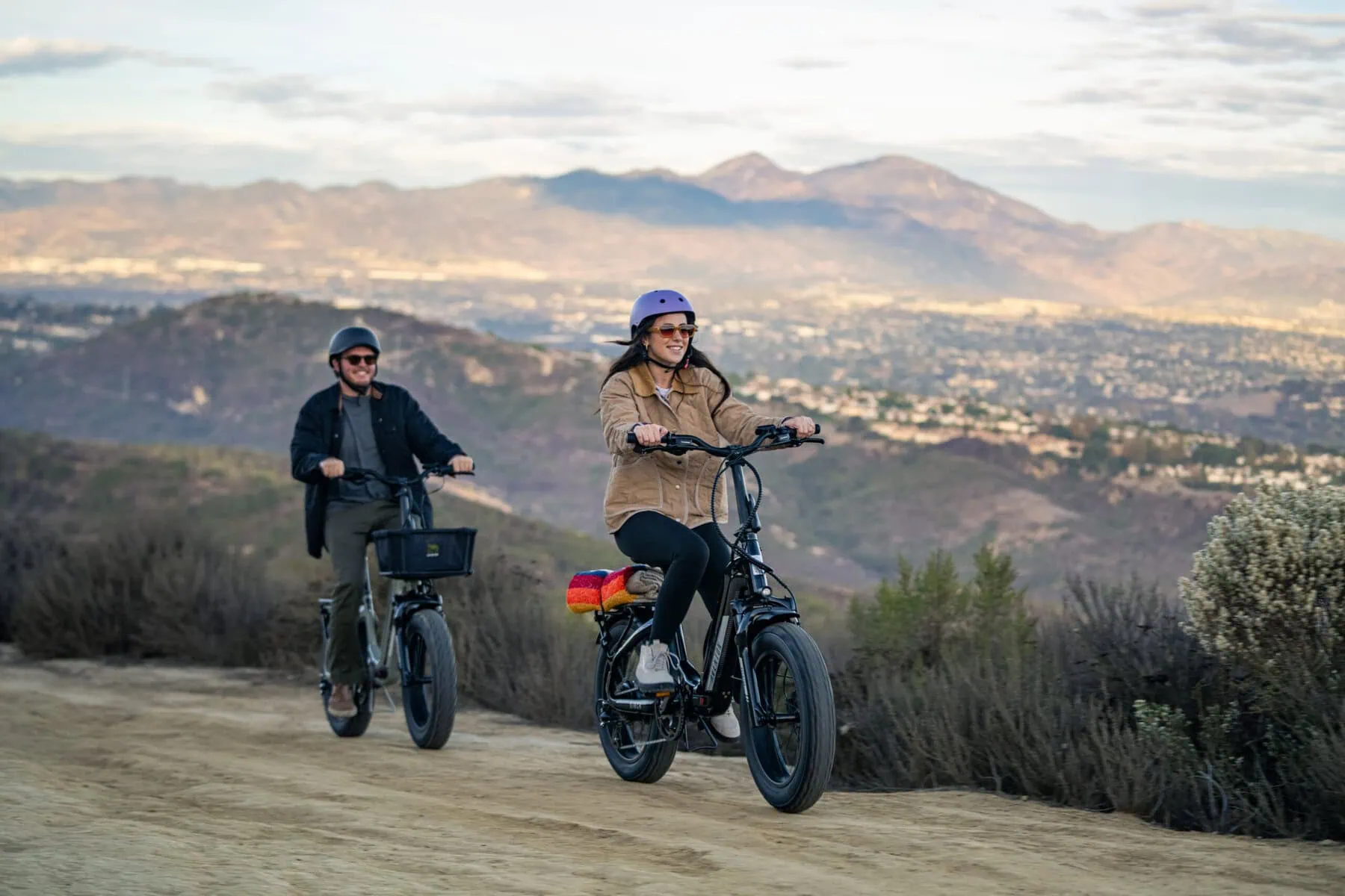 a man and woman riding e-bikes on a dirt road