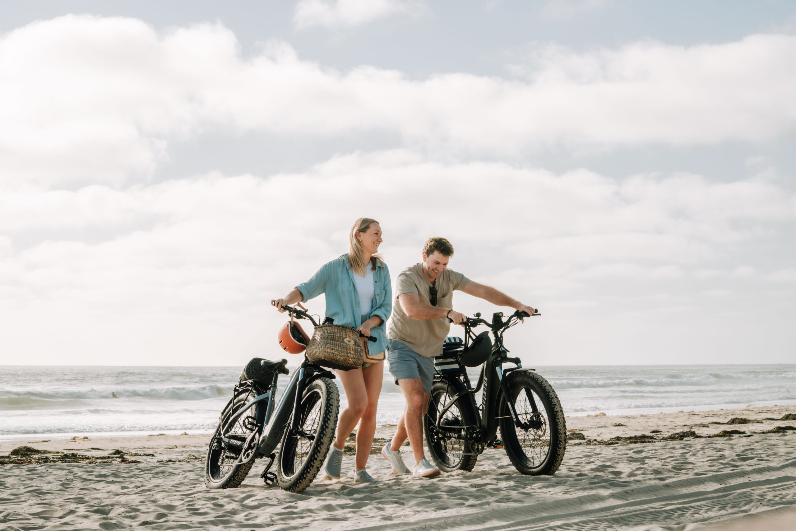 a man and woman standing on a beach with e-bikes