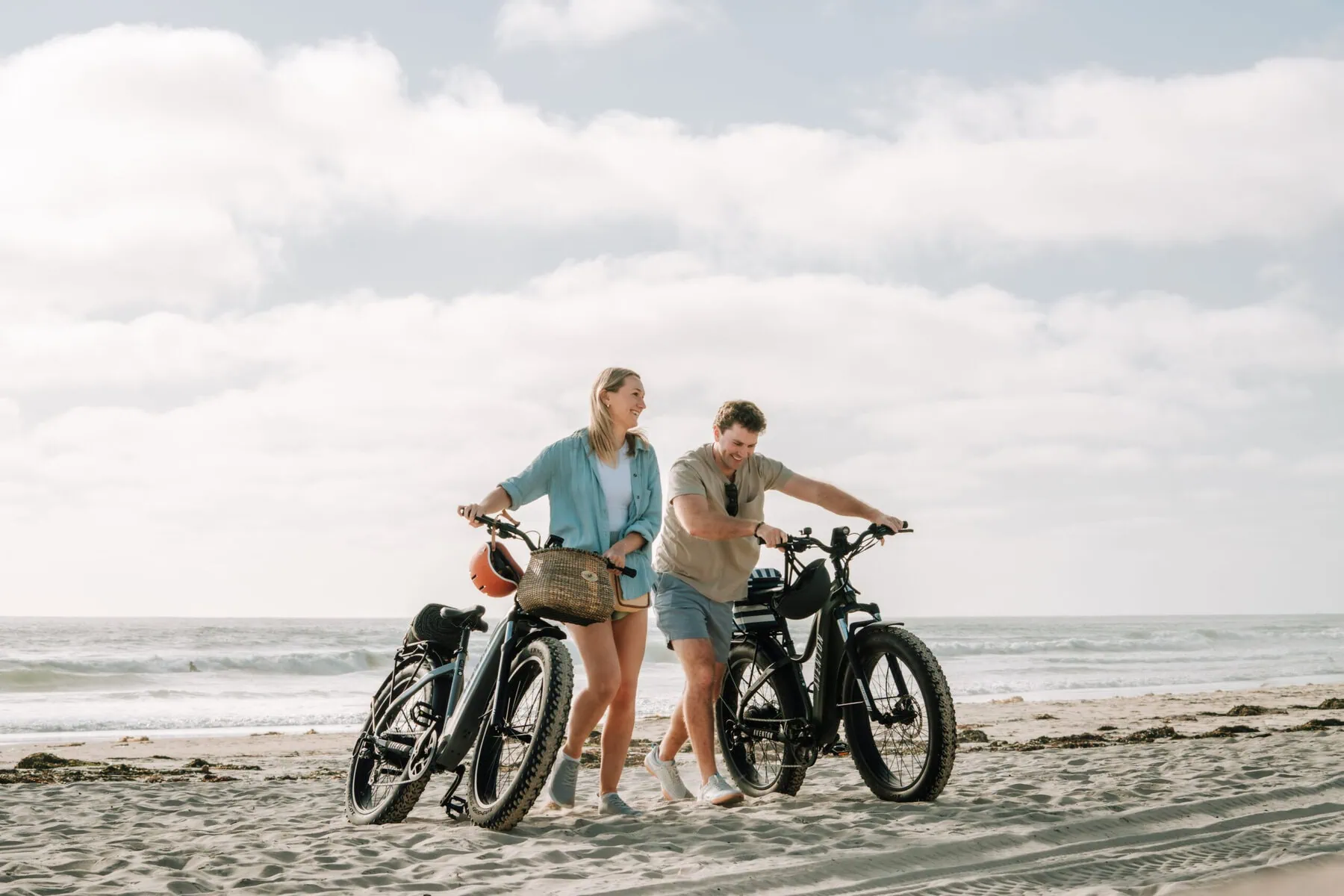 a man and woman standing on a beach with e-bikes