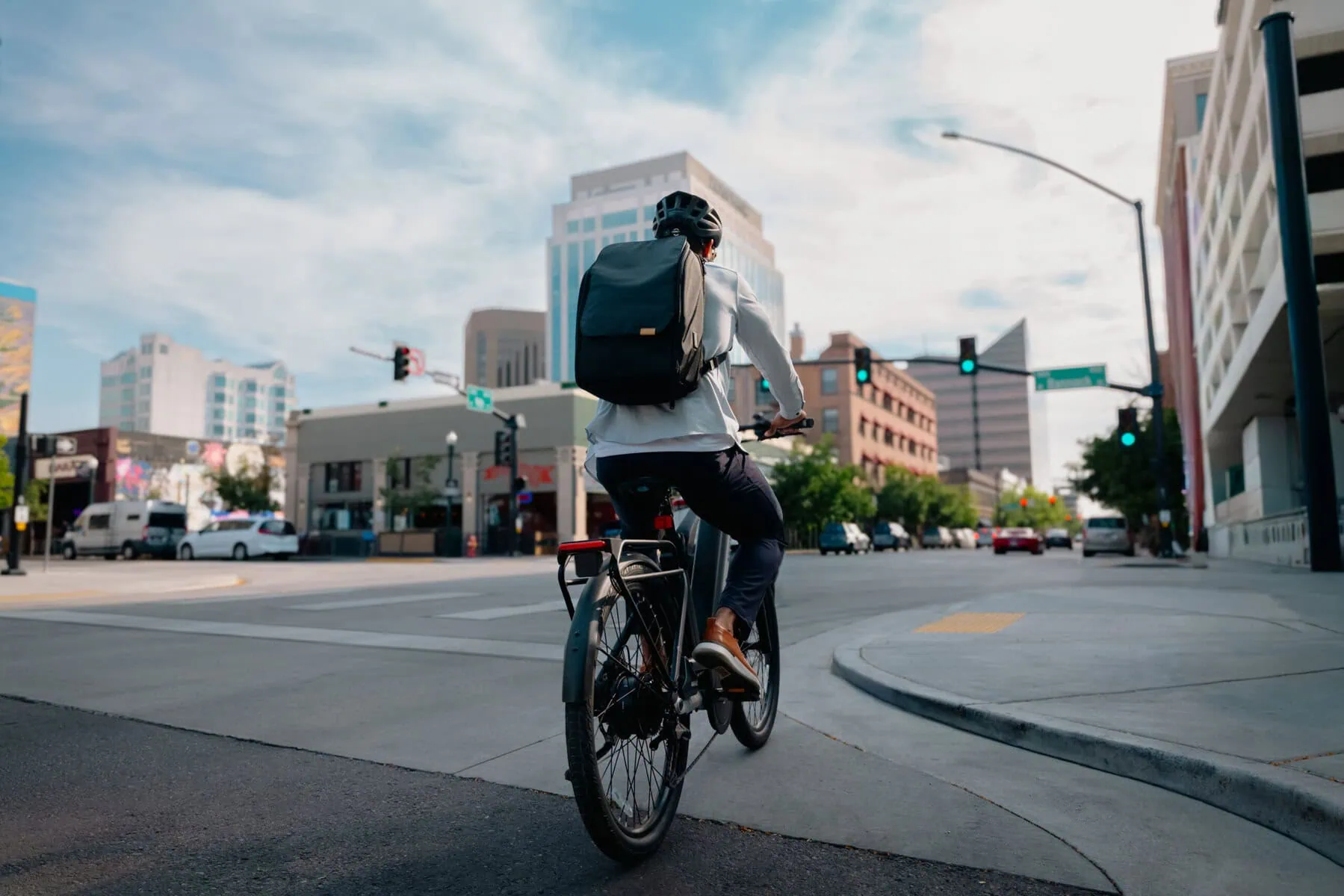 Segway Myon Ebike Grey back right side view of man riding with backpack on the city road towards to traffic light between buildings