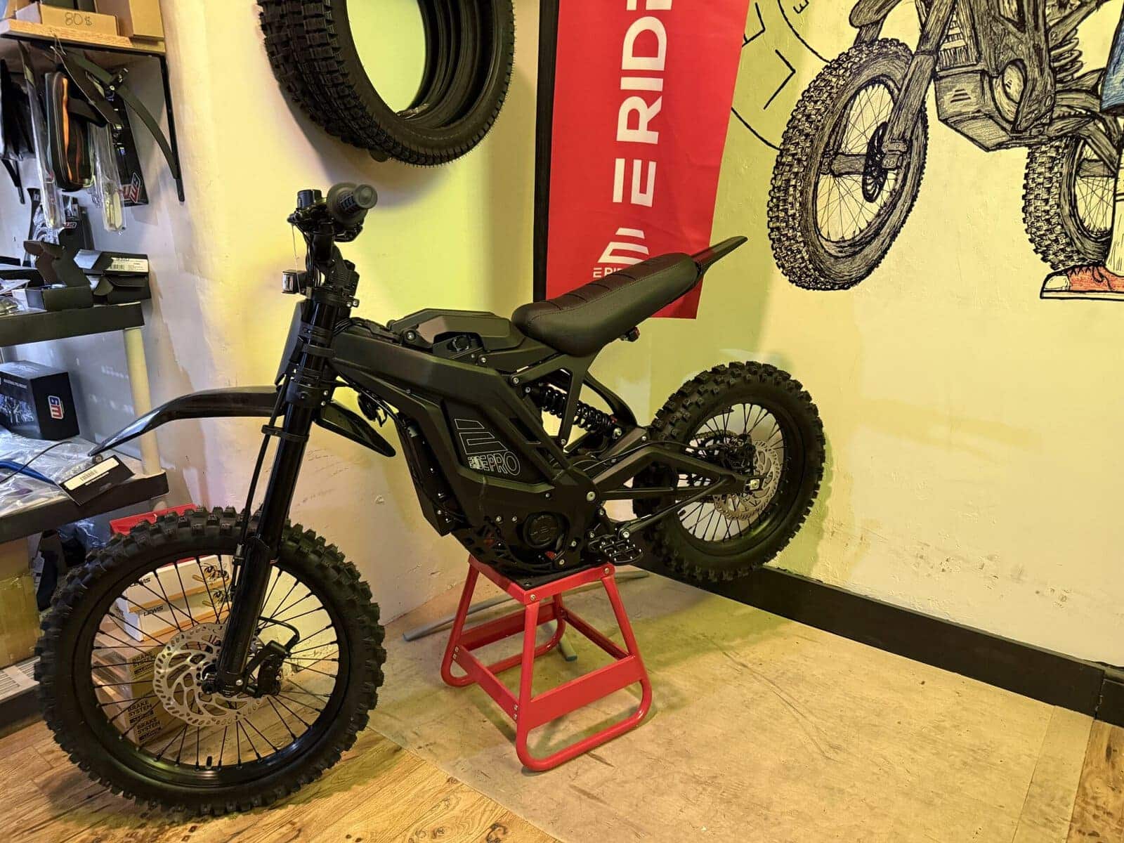 E Ride Pro electric dirt bike on display stand inside Let's Roll Lancaster with shop mural