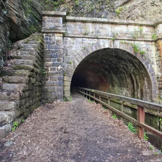 Stone arch tunnel entrance on the C and O Canal Towpath, with a wooden railing along the dirt path