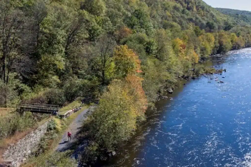 Aerial view of the D and L Trail following a river through a wooded valley, with a cyclist on the path