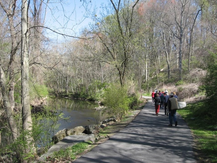 Group walking the paved Darby Creek Trail beside the creek on a clear early spring day