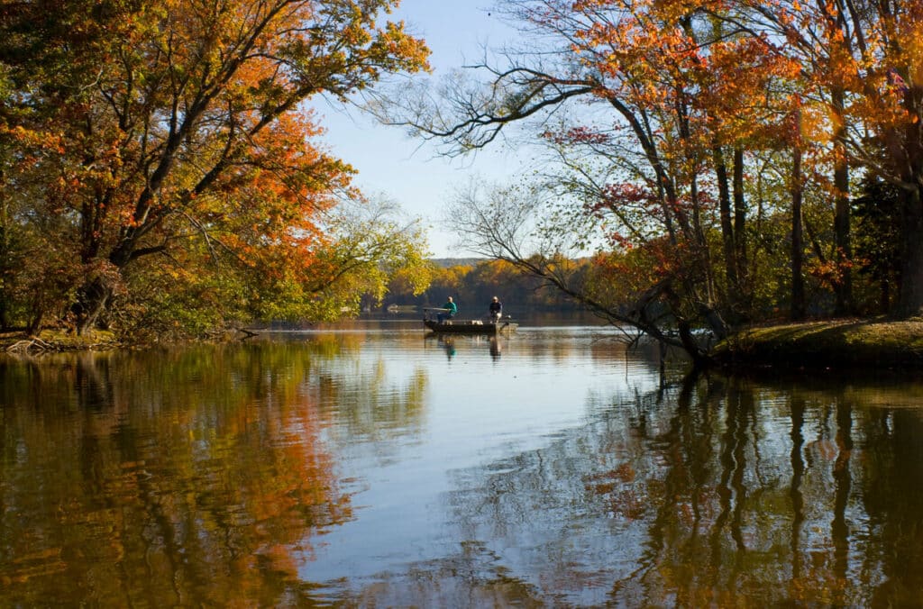 Two people in a boat on a French Creek State Park lake ringed by orange and yellow fall foliage